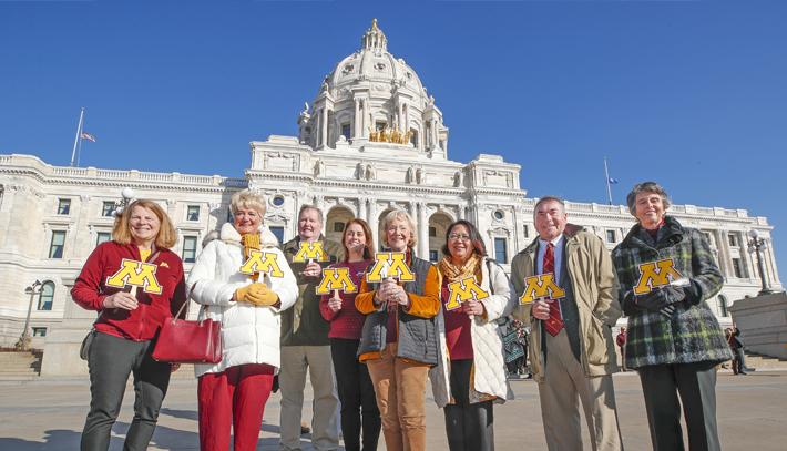 Members of the Board of ɫС holding a block M sign and standing in front of the state capitol